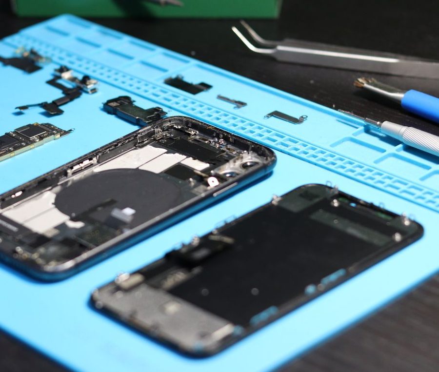 Repuestos de celular sobre una manta de trabajo: chasis, módulo de pantalla, flex y herramientas de precisión.